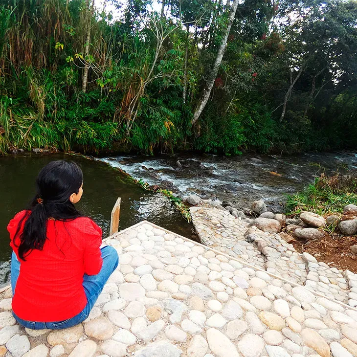 Nuestra viajera disfruta de un momento de tranquilidad, sentada en el borde de la poza natural, rodeada por la belleza de la naturaleza.